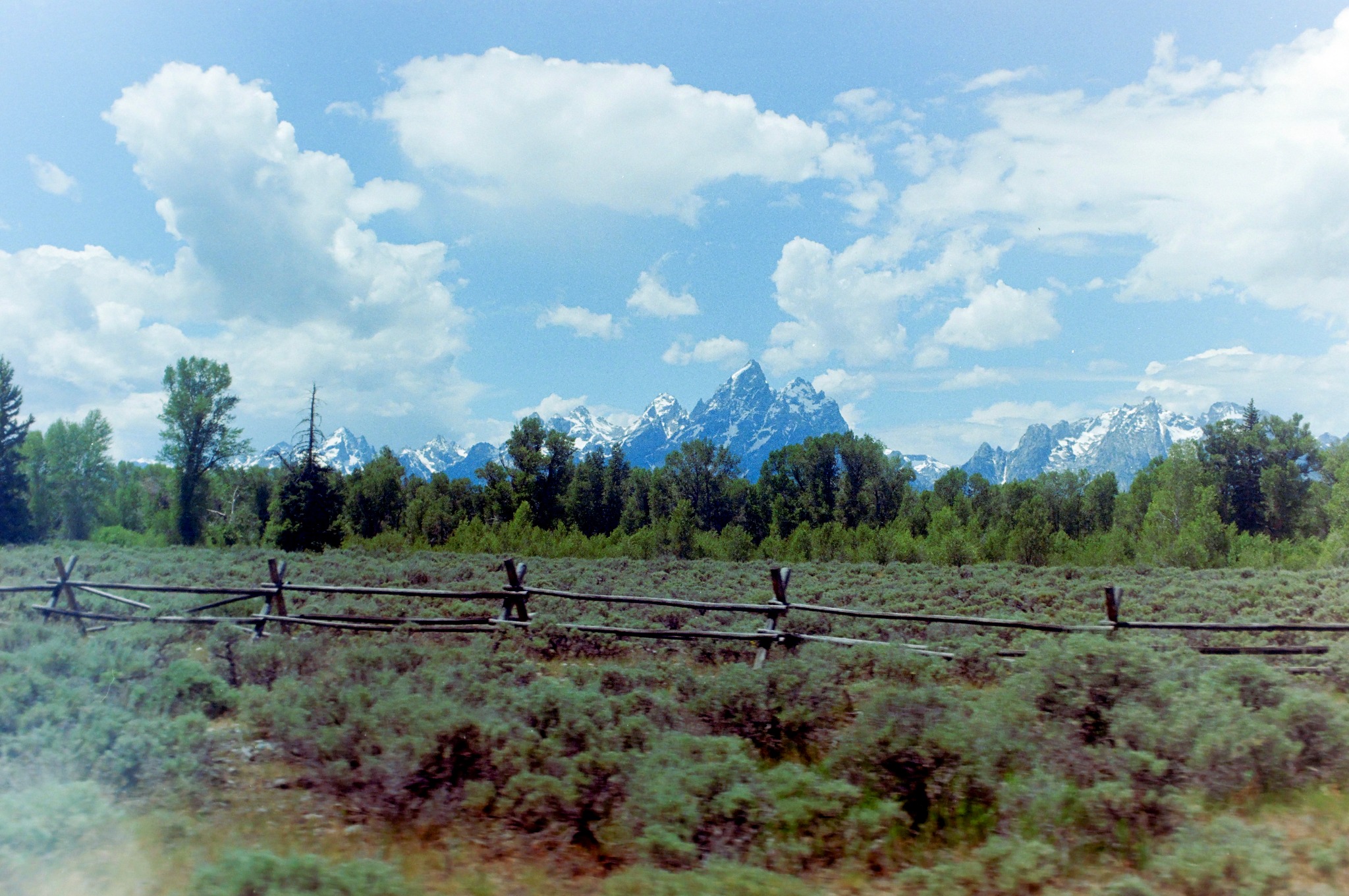 Snowcapped Tetons beyond a split rail fence