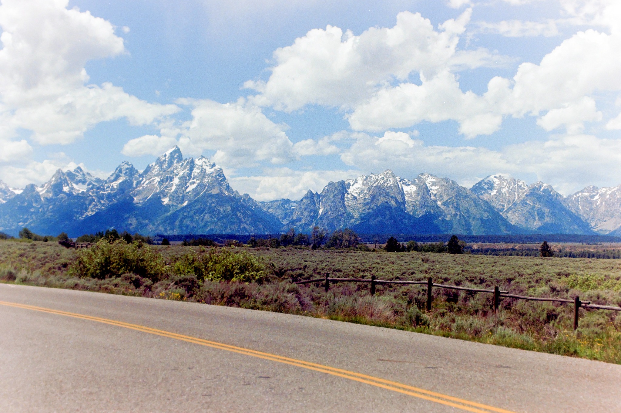 Grand Teton mountain range beyond a roadside fence and highway
