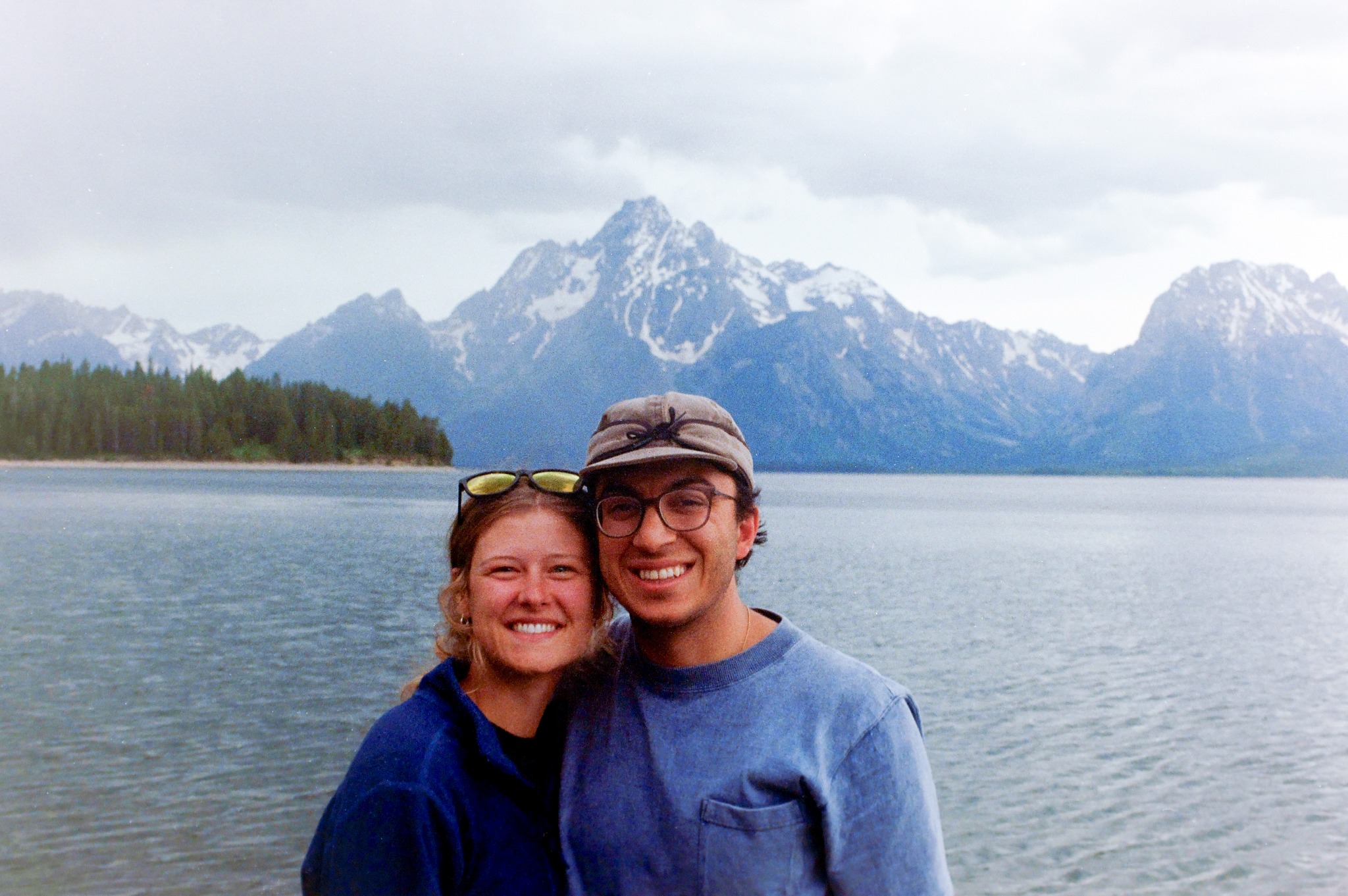 Two people smiling beside a lake with the Tetons behind them